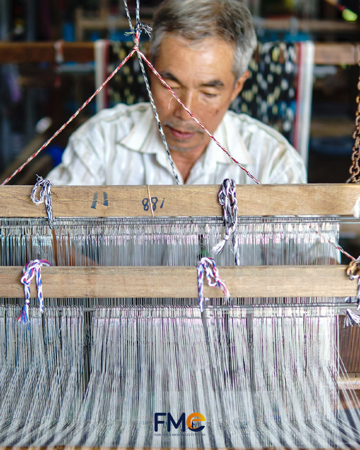 An elderly man is weaving handmade cloth with loom