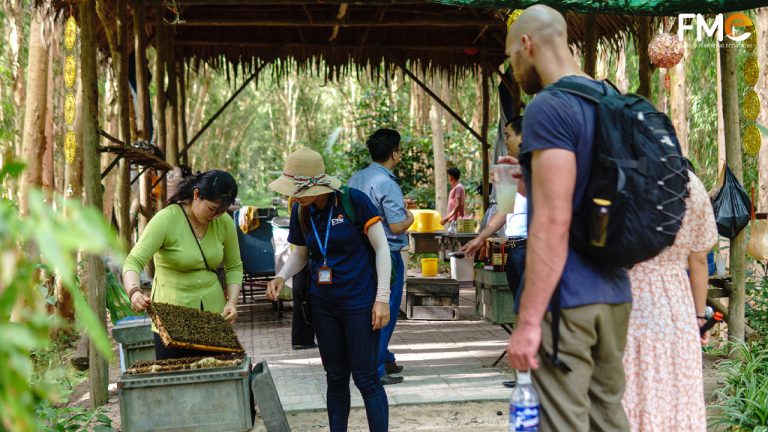 A woman is holding a beehive to showcase to the tourists and tour guide