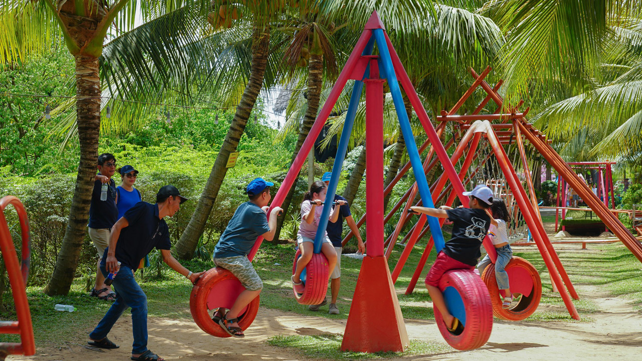 Parents play on swings with children at Con En Lugar eco-tourism area in An Giang