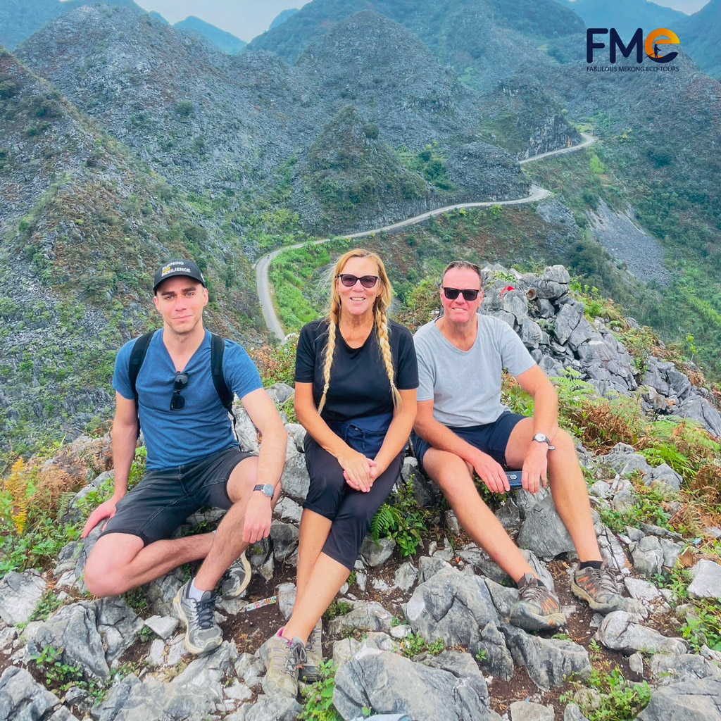 A family sitting on rocky terrain, with the breathtaking Dong Van karst plateau and meandering roads in the distance