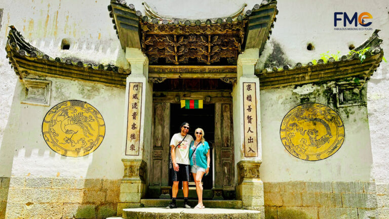 A couple poses at the entrance of the Hmong King Palace, showcasing its intricate architecture and cultural heritage amidst a sunny day