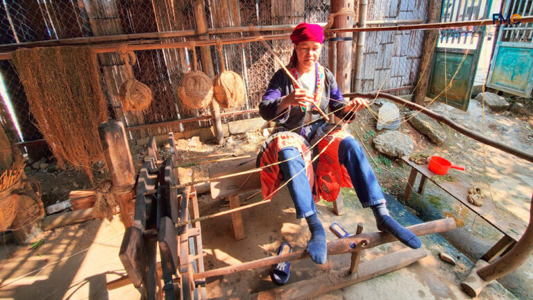 An ethnic woman diligently weaving on a traditional loom under the shade of corn husks, a beautiful depiction of the craftsmanship of Lung Tam Village