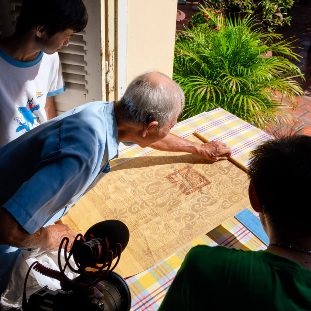 An elderly man examining an ancient scroll with detailed patterns at Le Cong Ancestral House