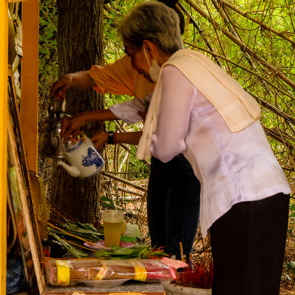 A senior woman performing water offerings during a Buddhist ceremony in Vietnam