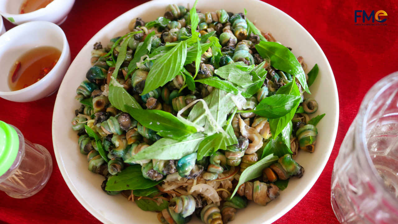 A flavorful snail salad dish served with fresh herbs at Dung Islet in the Mekong Delta, Vietnam