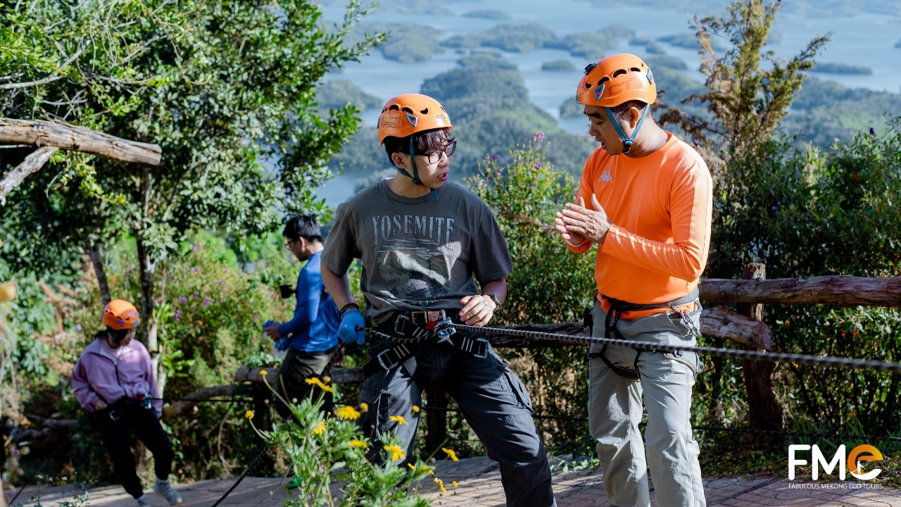 An expert instructor providing one-on-one abseiling safety training and gear checks for a guest overlooking the Ta Dung Lake islands.