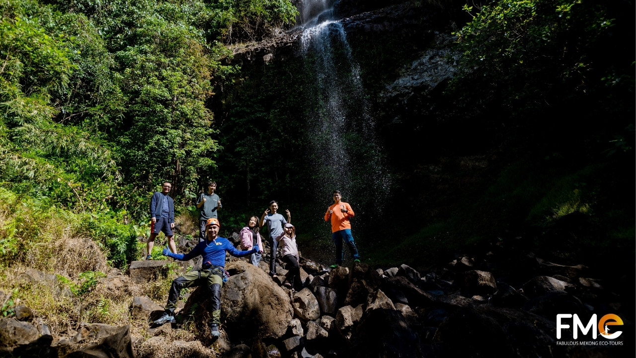Happy group posing at the rocky base of Ta Dung waterfall after completing the canyoning challenge.