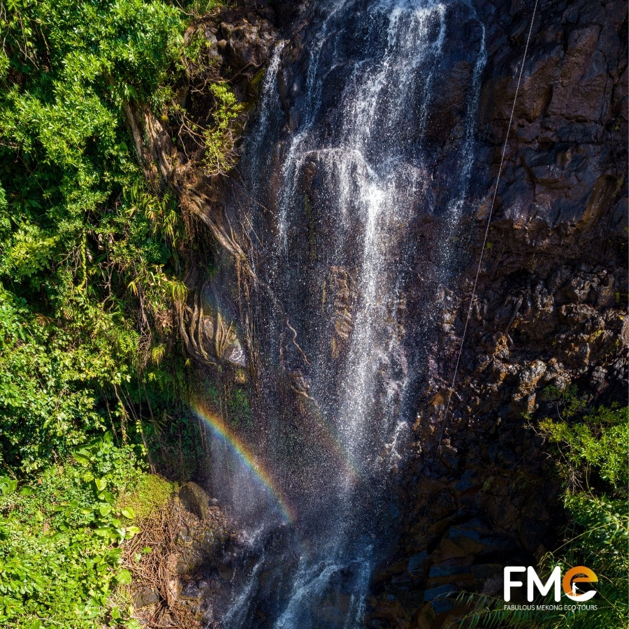 A breathtaking aerial view of the majestic Ta Dung waterfall with a vibrant rainbow forming in the mist at the base.