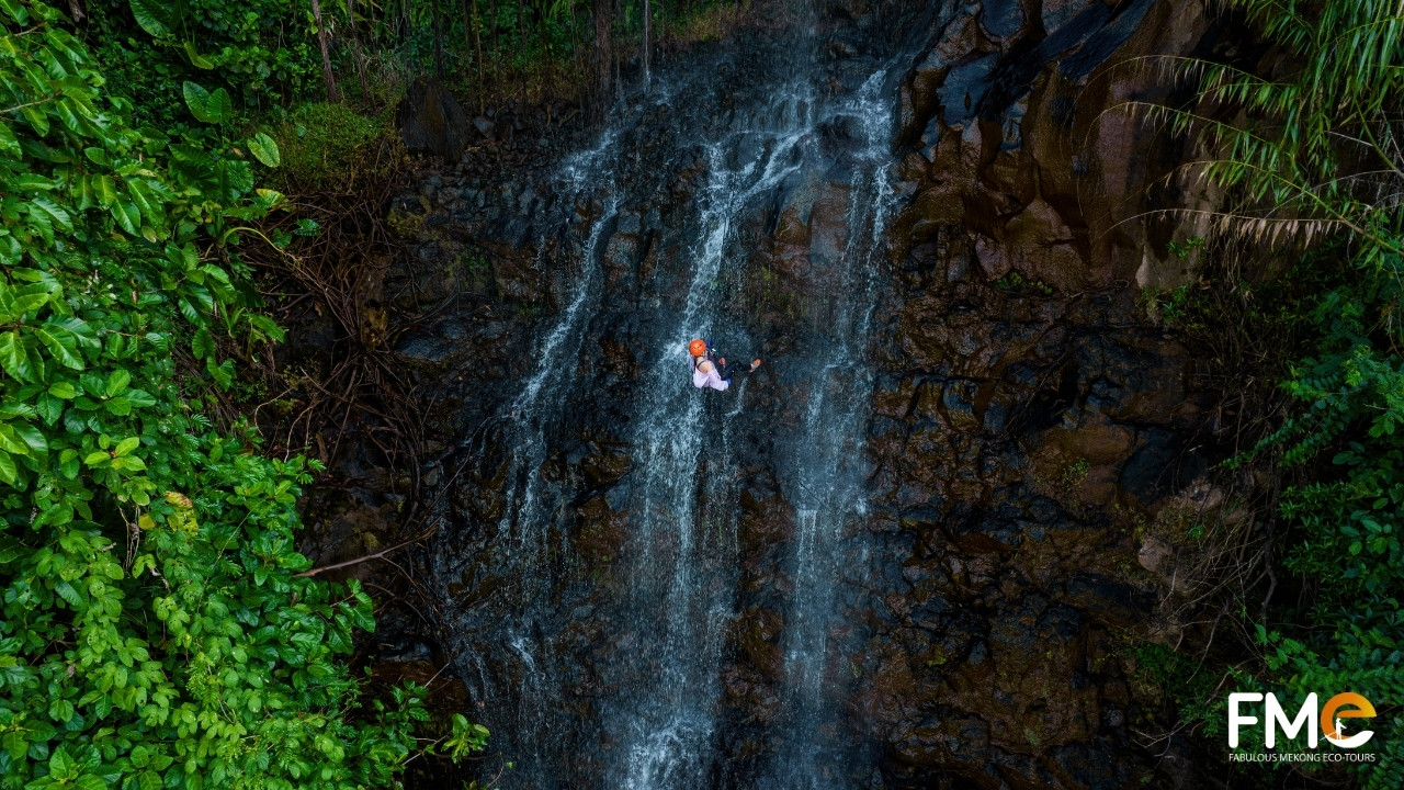 A spectacular high-angle shot of a solitary explorer abseiling down the massive Ta Dung waterfall, emphasizing the scale of nature vs human.