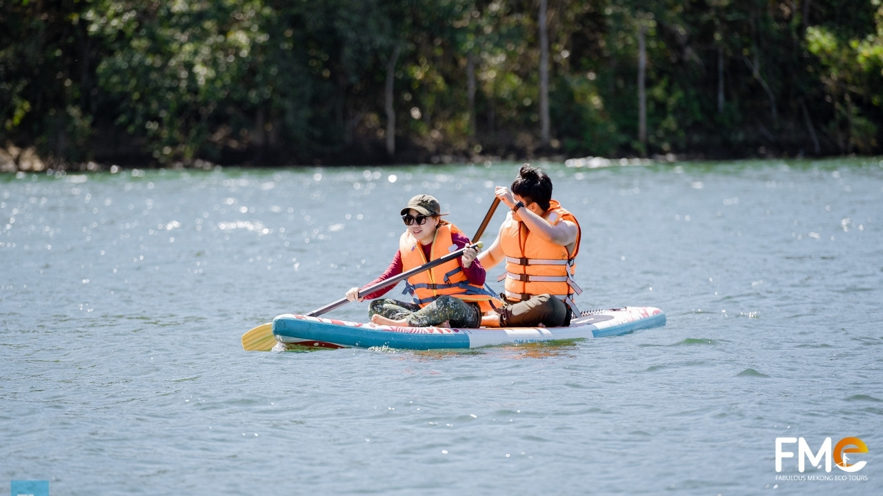 Travelers enjoying a fun Stand-Up Paddle (SUP) boarding session on the emerald waters of Ta Dung Lake.