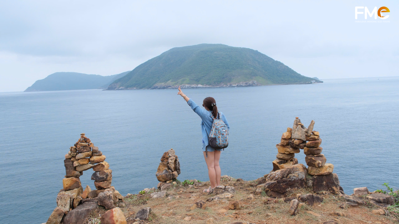 FME Travel tour group posing happily on a scenic coastal path overlooking the turquoise waters and distant islands of Con Dao, Vietnam.