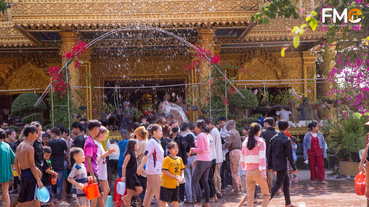 Youth joyfully splashing water on each other in the courtyard of a Khmer pagoda featuring gilded architecture.