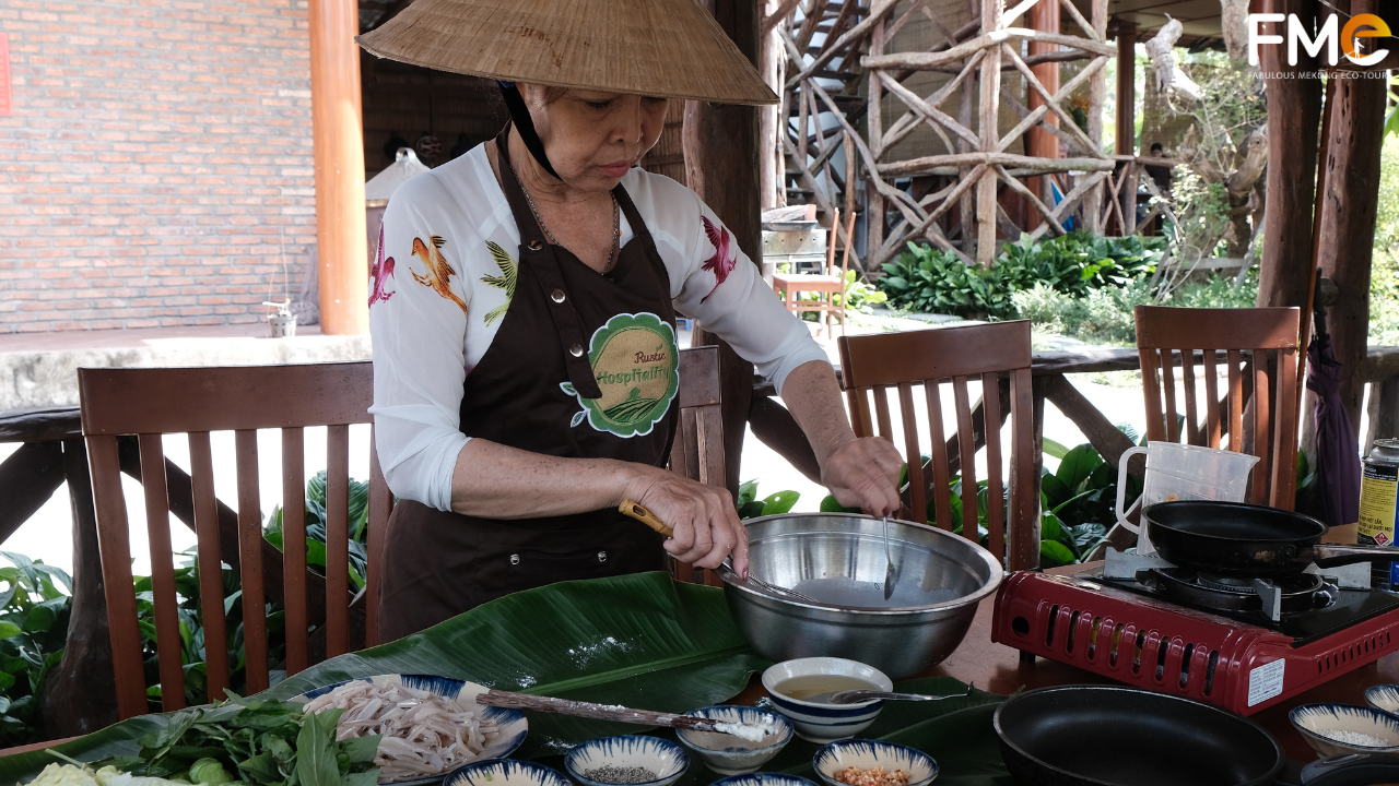 A local chef in a traditional conical hat mixing the light flour batter in a rustic outdoor kitchen setting.